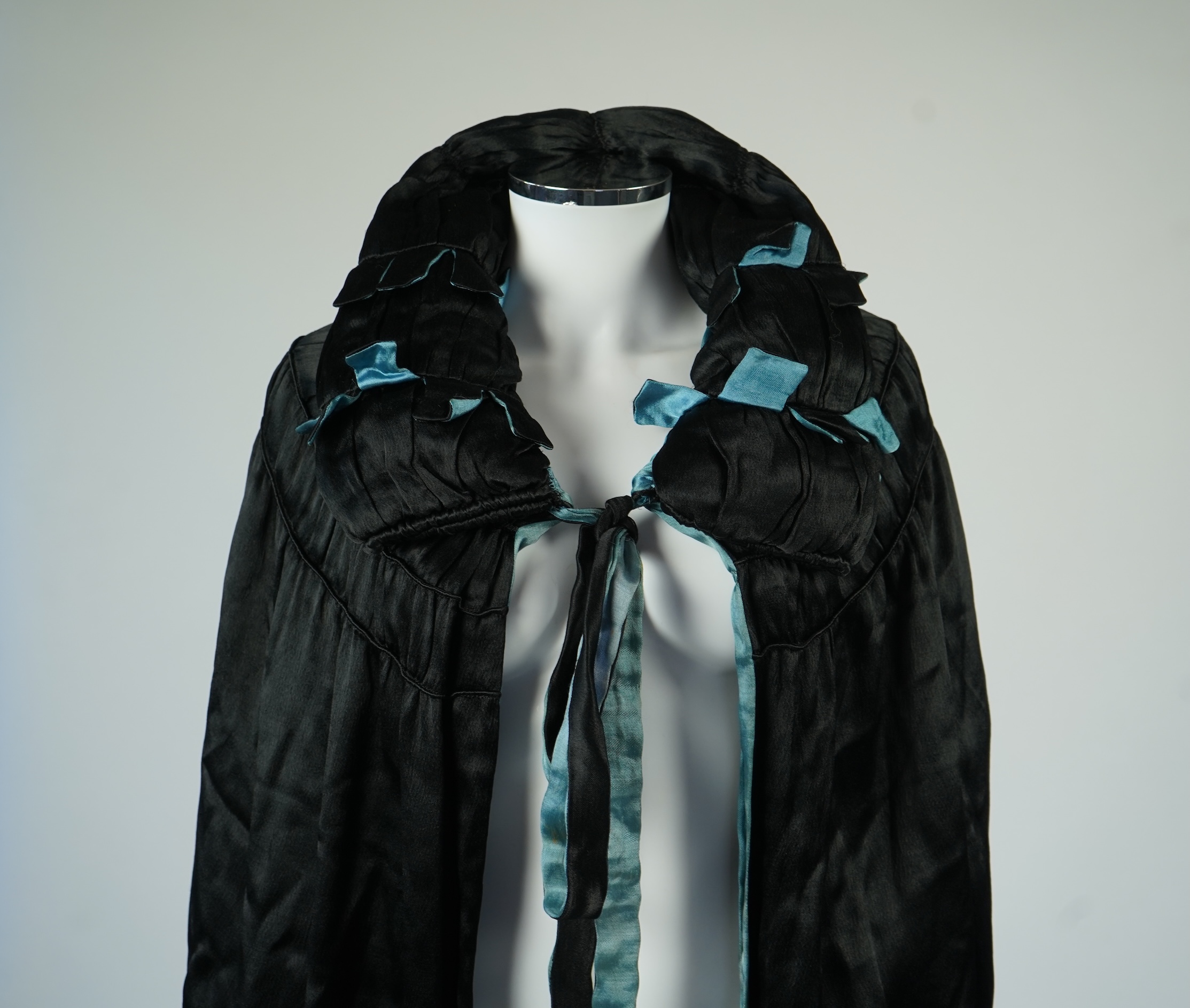 A 1920's ladies blue lined, black silk opera cape. Designed with a rushed ornate collar and scalloped and fringed lower edge. 95cm long fron neck to base. Condition - stained near the front edge, possibly removable with
